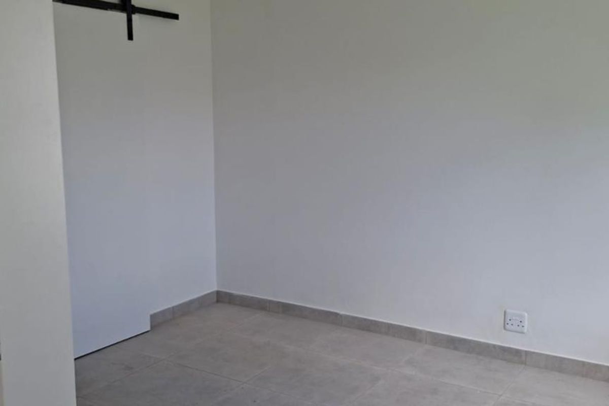 An empty bedroom featuring neutral tiled flooring, white walls, and a sliding door track, ready for personalization.
