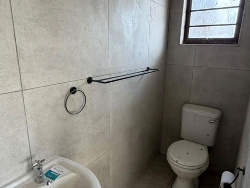 A functional bathroom featuring tiled walls, a standard toilet, and a washbasin with modern black hardware accessories.