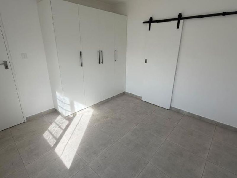 A bright, empty bedroom featuring neutral tiled flooring, ample built-in cupboard storage, and a modern sliding barn door.