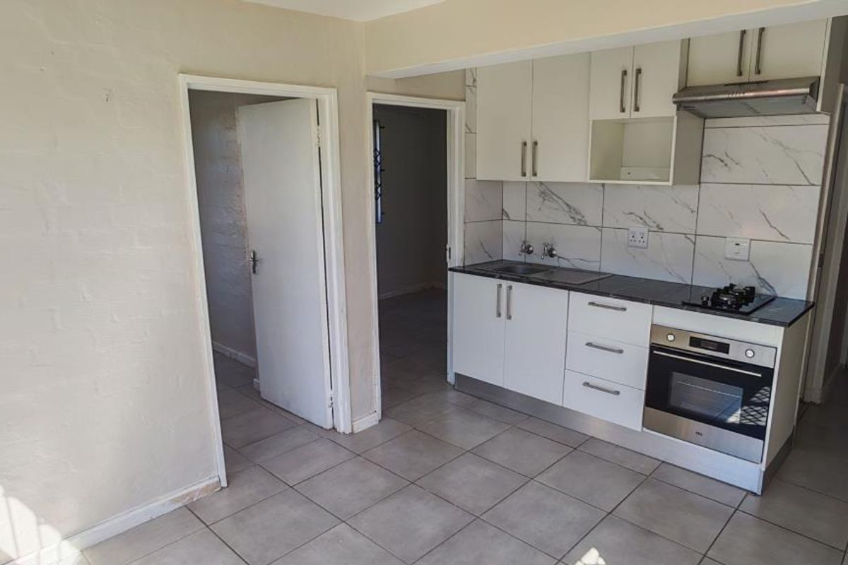 Compact kitchen featuring white cabinetry, stainless steel oven, gas hob, extractor fan, and marble-look tiled backsplash with neutral floor tiles.