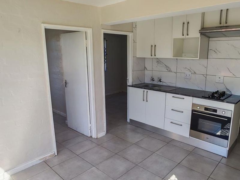 Compact kitchen featuring white cabinetry, stainless steel oven, gas hob, extractor fan, and marble-look tiled backsplash with neutral floor tiles.