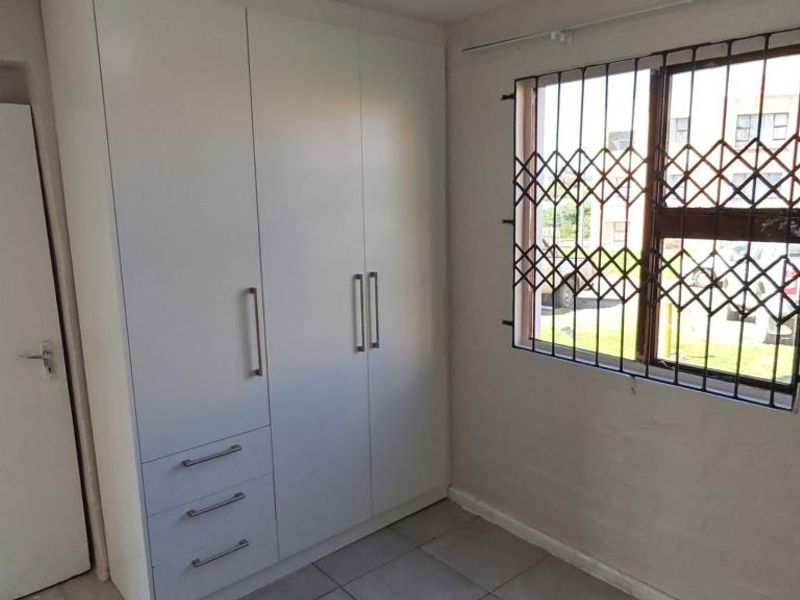 A clean, empty bedroom featuring built-in cupboards, tiled flooring, and a window fitted with a security gate.