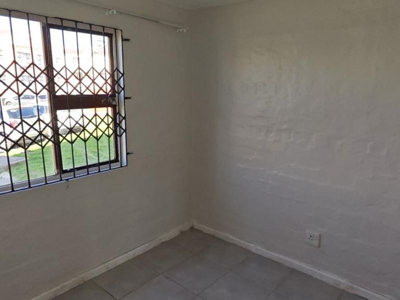 An empty bedroom featuring tiled flooring, a window with security bars, and plain painted walls.