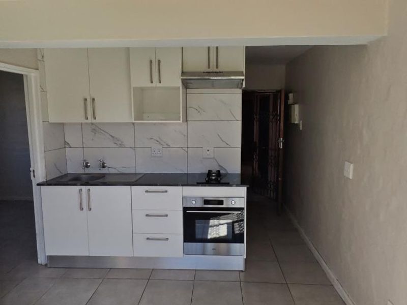 Compact kitchen featuring white cabinetry, marble-look tile backsplash, built-in oven, cooktop, and extractor fan with neutral tiled flooring.