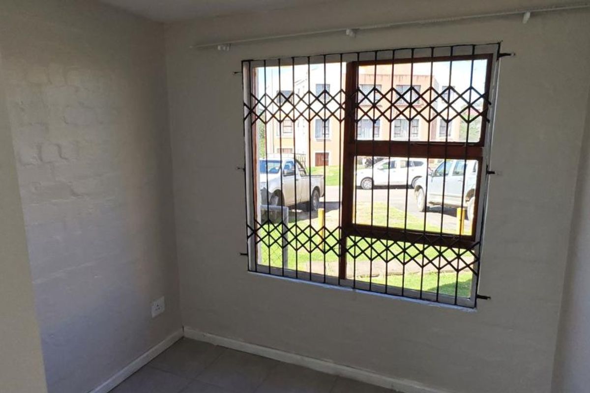An empty bedroom featuring tiled flooring and a window fitted with a security gate, offering a functional and secure living space.