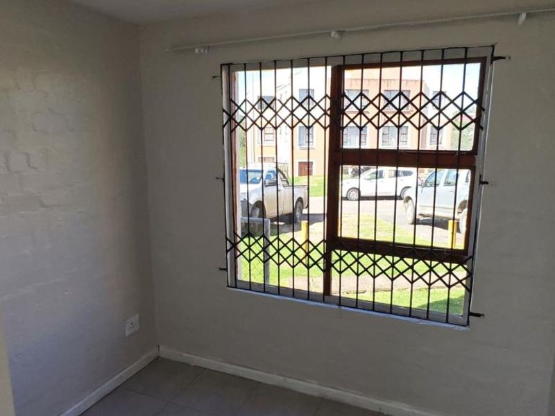 An empty bedroom featuring tiled flooring and a window fitted with a security gate, offering a functional and secure living space.
