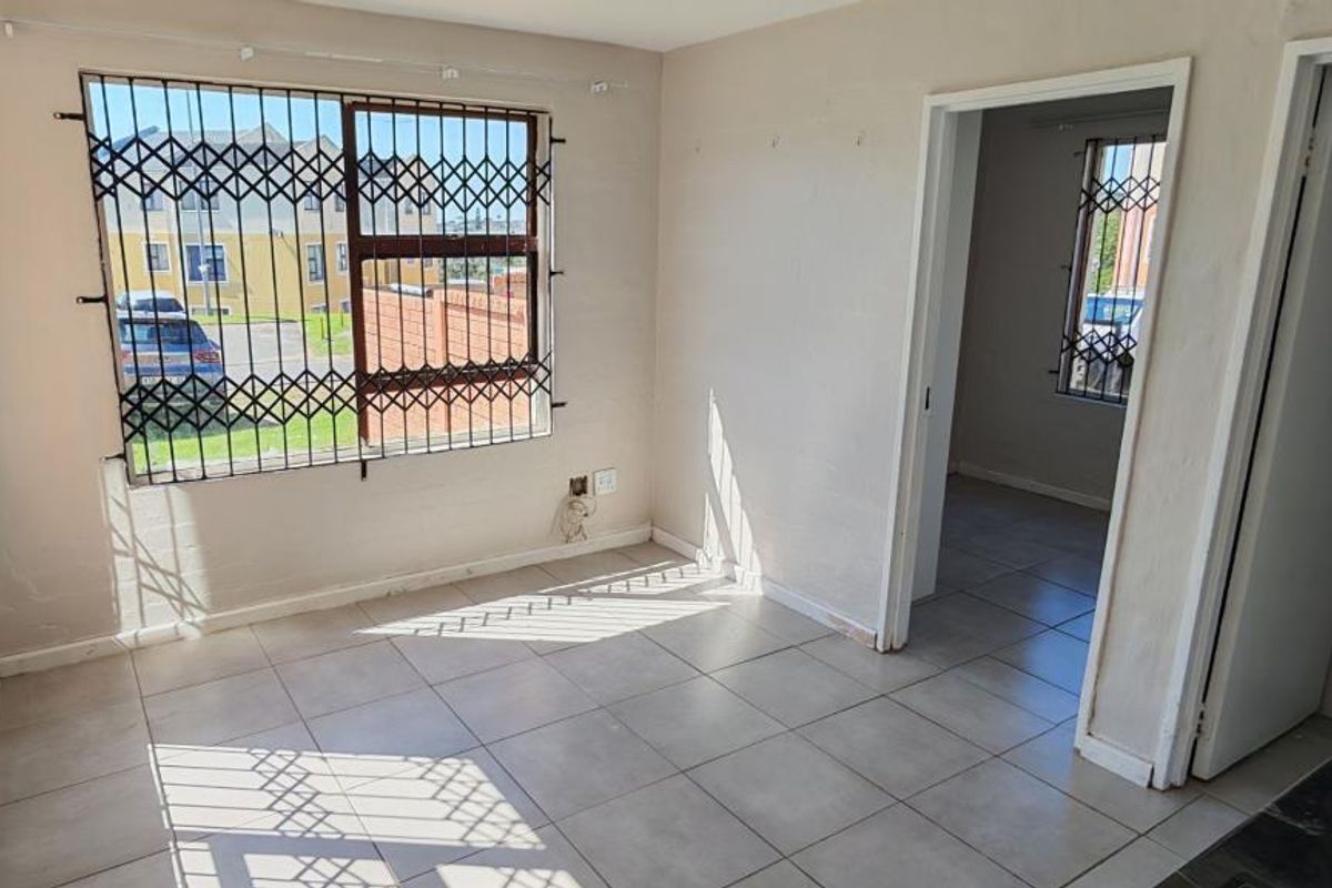 An empty living area featuring tiled flooring and security bars on the windows, offering a blank canvas for interior design.