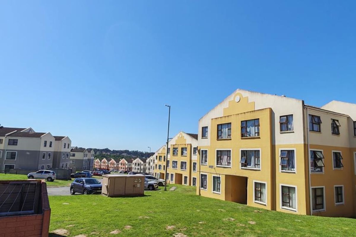 Exterior view of multi-story apartment complex featuring yellow and grey facades, paved parking areas, and surrounding green lawn spaces.