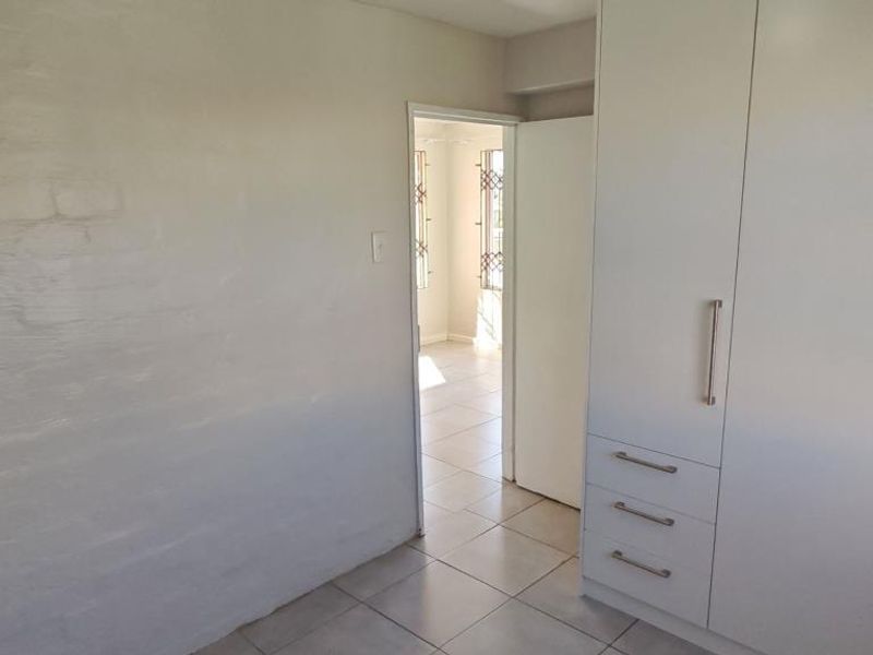 A clean, empty bedroom featuring built-in cupboards, neutral tiled flooring, and a view through to an adjacent room with security gates.