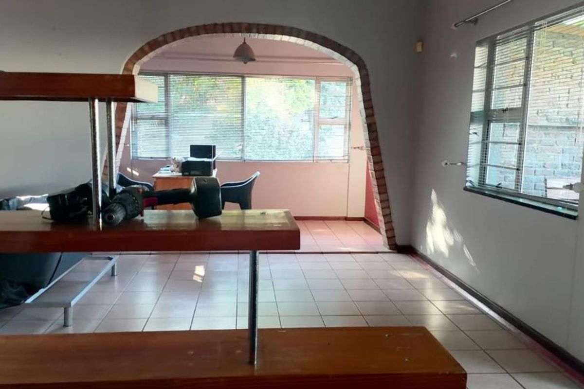 Spacious living area featuring a distinctive brick archway, tiled flooring, and large windows with venetian blinds, offering a versatile layout for renovation.