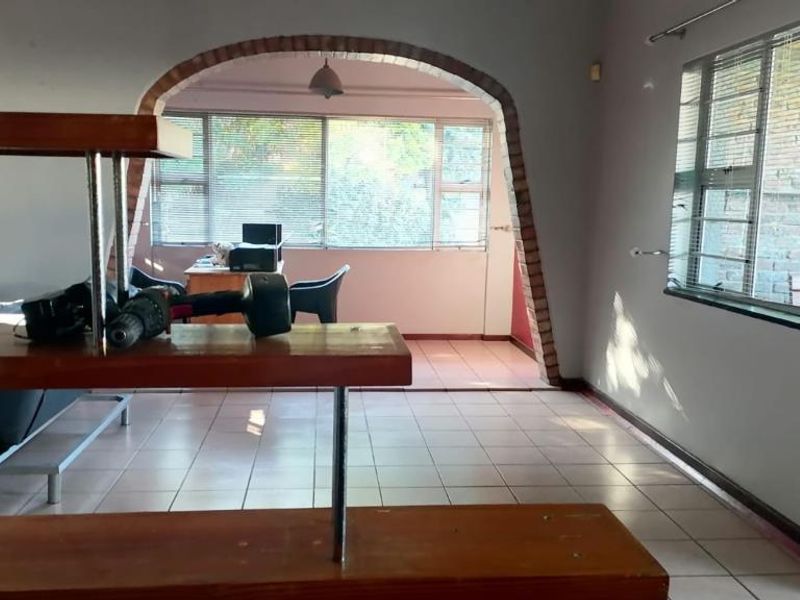 Spacious living area featuring a distinctive brick archway, tiled flooring, and large windows with venetian blinds, offering a versatile layout for renovation.