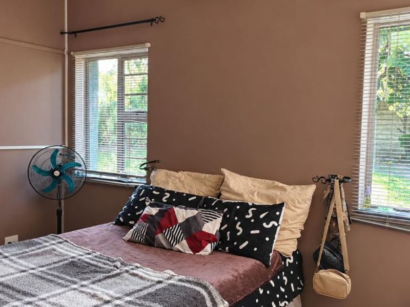 A bedroom featuring brown walls, aluminium window frames with venetian blinds, and visible electrical conduit running along the wall.