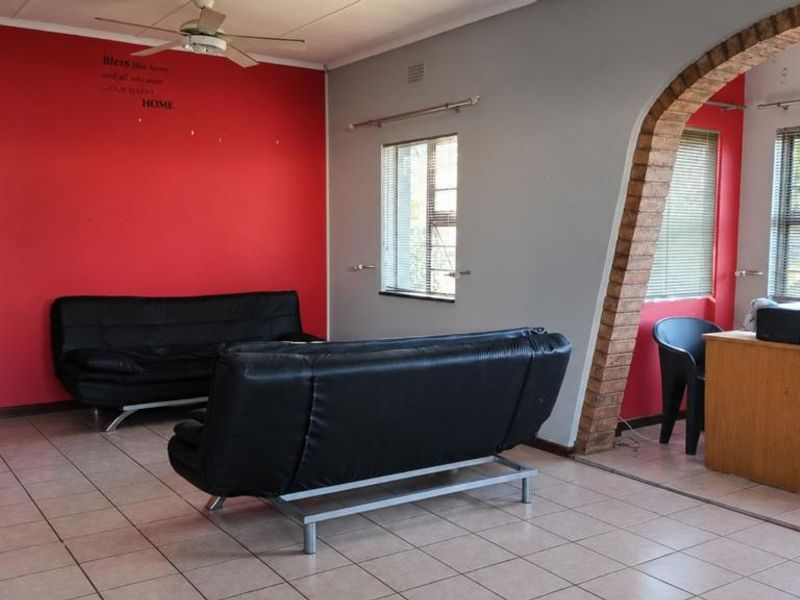 Spacious living area featuring tiled flooring, a distinctive brick archway, and large windows with venetian blinds, offering a versatile layout for family living.