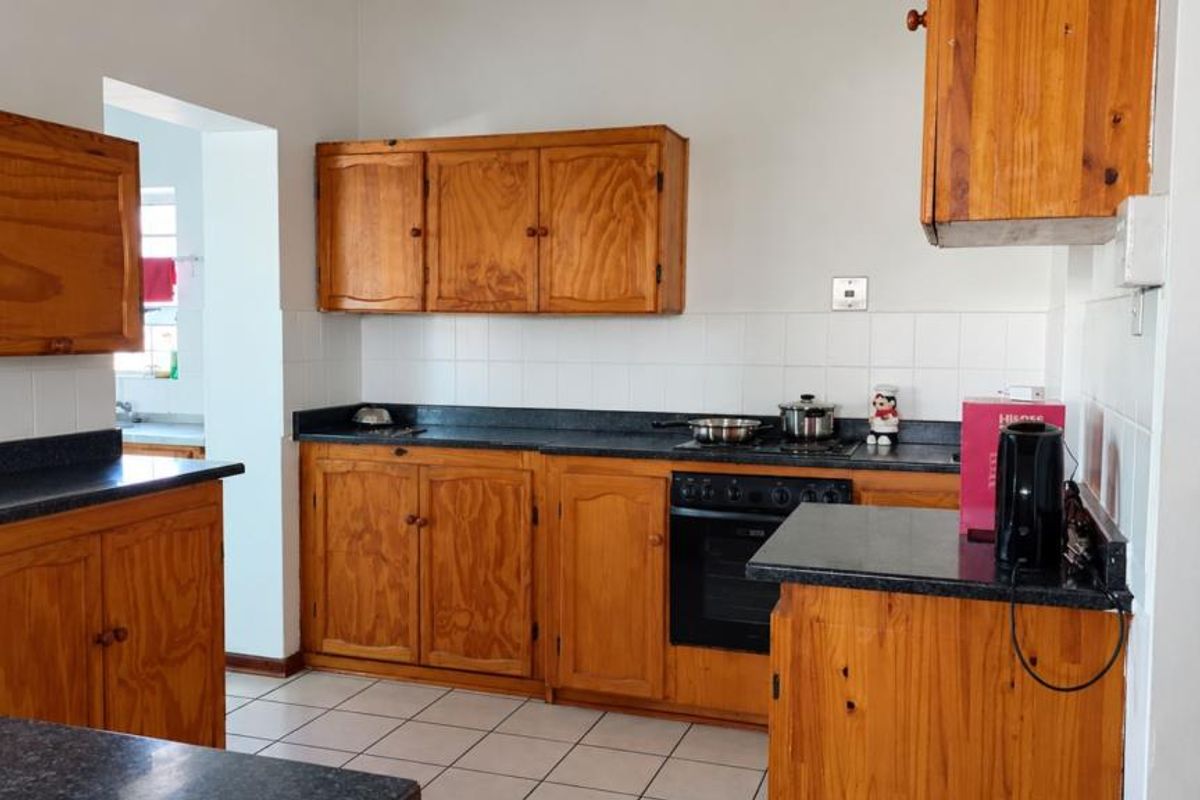 A functional kitchen featuring wooden cabinetry, dark laminate countertops, a built-in oven, and a tiled backsplash, offering a classic layout with potential for modernization.