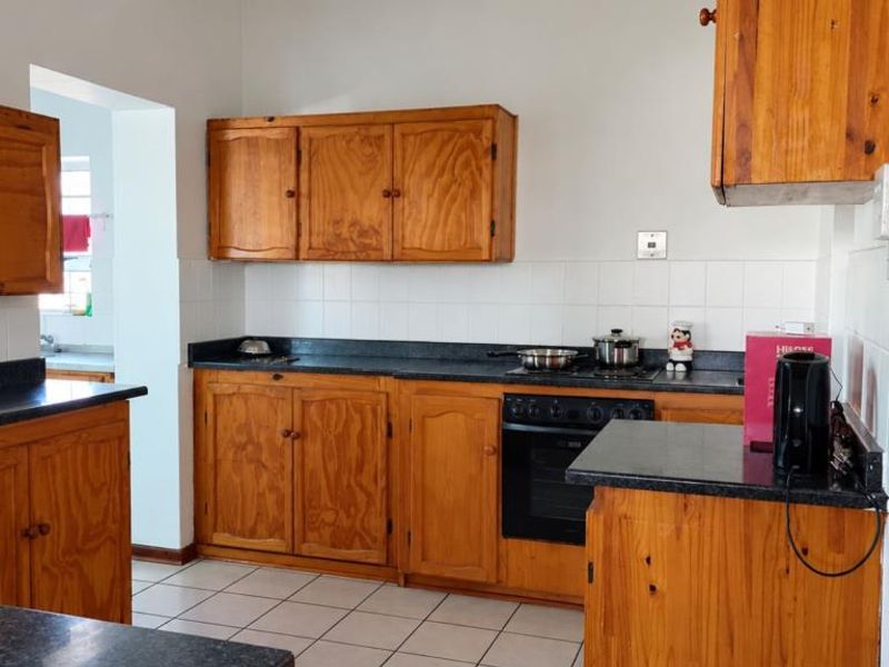A functional kitchen featuring wooden cabinetry, dark laminate countertops, a built-in oven, and a tiled backsplash, offering a classic layout with potential for modernization.