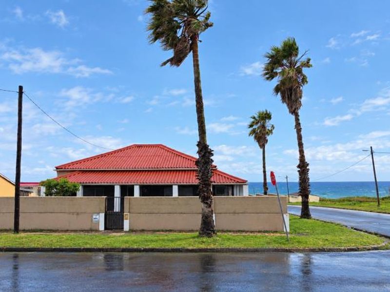 Front exterior view of a coastal property featuring a perimeter wall, gated entrance, and a tiled roof, situated near the ocean.