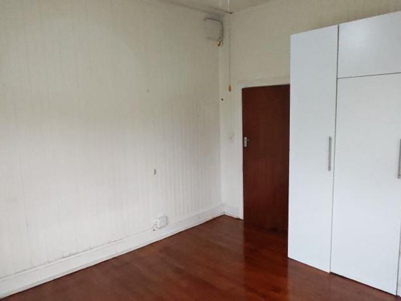 A bedroom featuring timber flooring, white wall paneling, and a large built-in wardrobe with modern white cabinetry.