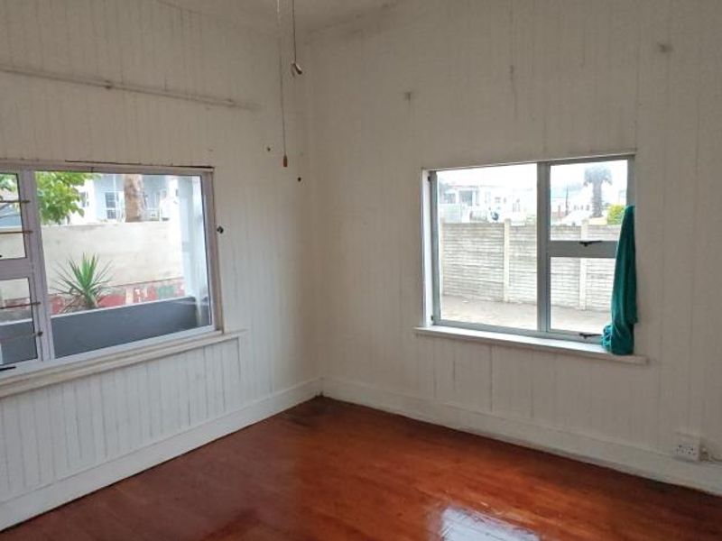 An empty bedroom featuring timber flooring and white timber wall paneling with aluminium-framed windows.