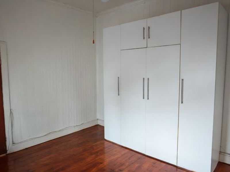 A vacant bedroom featuring timber flooring, white wall paneling, and a large built-in wardrobe with overhead storage.