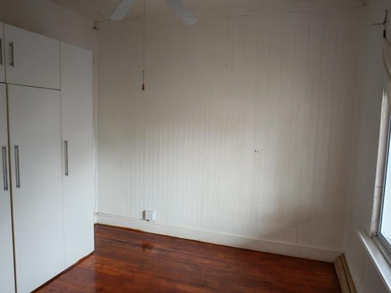 A vacant bedroom featuring timber flooring, built-in cupboards, and timber wall paneling, offering a blank canvas for potential updates.