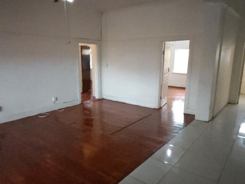 An empty open-plan living area featuring a combination of hardwood and tiled flooring, providing a blank canvas for renovation and interior design.