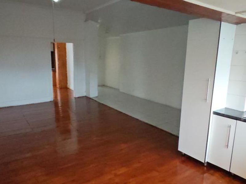 An open-plan living and kitchen area featuring hardwood and tiled flooring, with built-in kitchen cabinetry and a stainless steel sink.