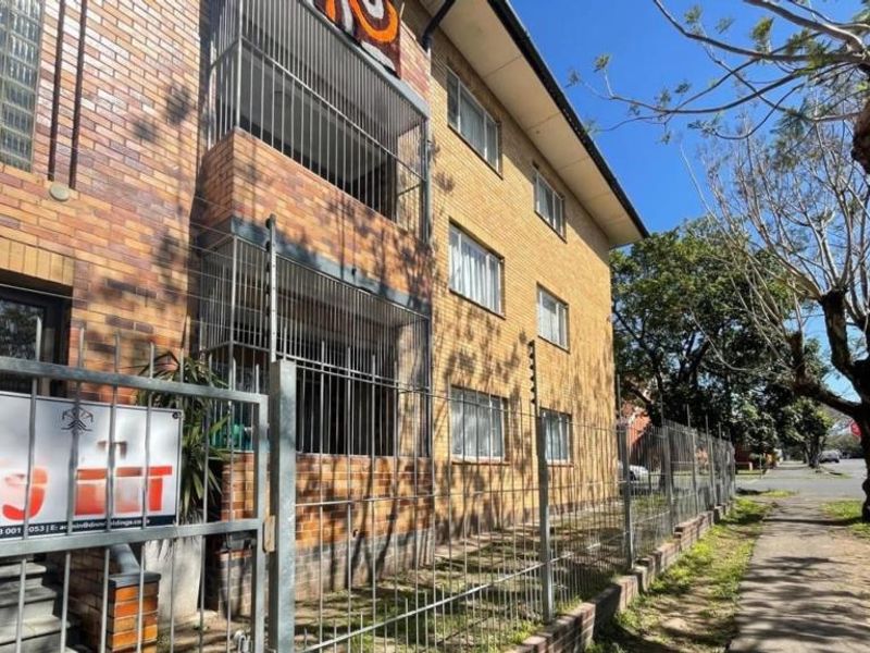 Front exterior view of a multi-story brick apartment building featuring security fencing, gated access, and balconies.