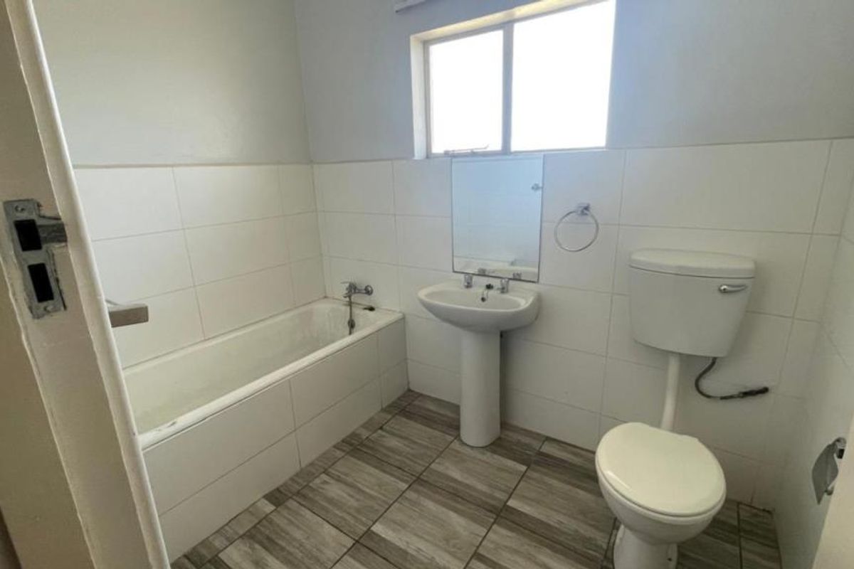 A functional bathroom featuring a pedestal basin, bathtub, and toilet with neutral wall and floor tiling, offering a clean and simple layout.