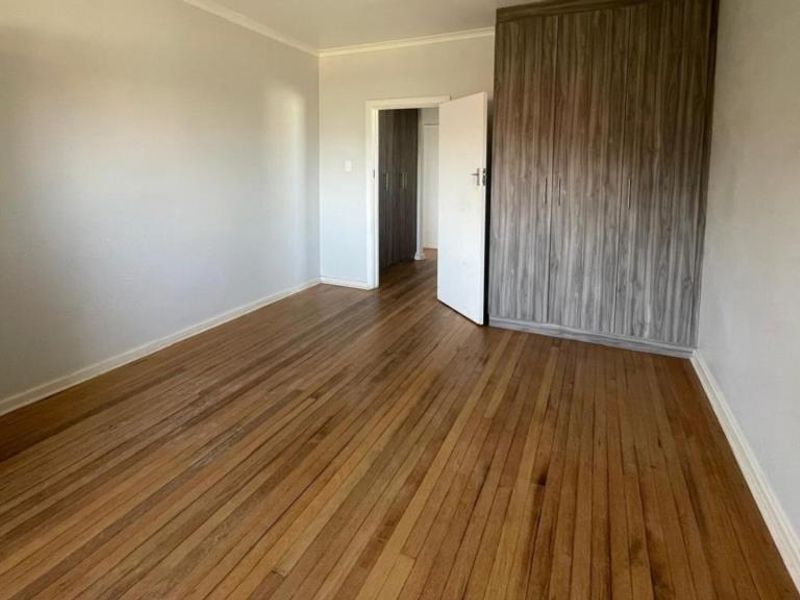 A spacious, empty bedroom featuring polished hardwood flooring and modern built-in cupboards, offering a clean and neutral canvas for personalization.