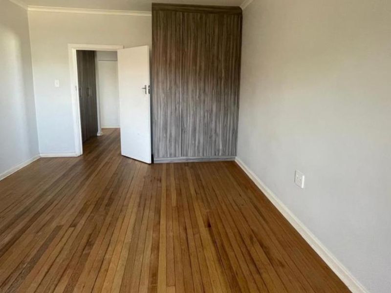 A bright, empty bedroom featuring polished wooden flooring and modern built-in cupboards, offering a clean and neutral space ready for personalization.