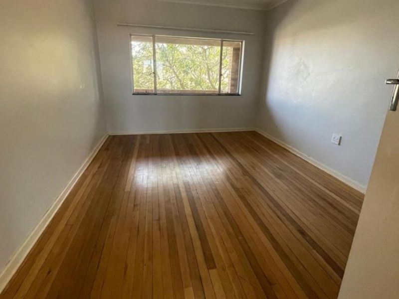 An empty bedroom featuring original hardwood flooring and a large window, providing a blank canvas for personalization.