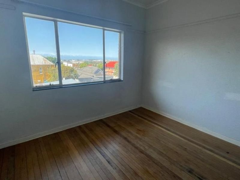 An empty bedroom featuring original timber flooring, a large window with neighborhood views, and classic picture rail detailing.