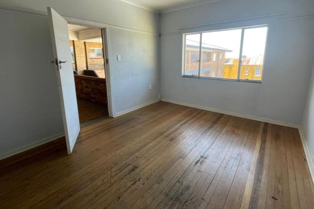 An empty bedroom featuring original hardwood flooring and a large window, offering a blank canvas for renovation or interior design updates.