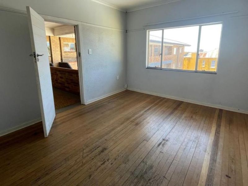 An empty bedroom featuring original hardwood flooring and a large window, offering a blank canvas for renovation or interior design updates.