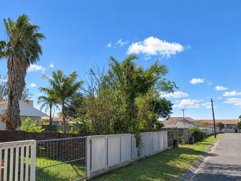 A street view showing the residential property boundary, perimeter fencing, and surrounding neighborhood infrastructure under a clear blue sky.