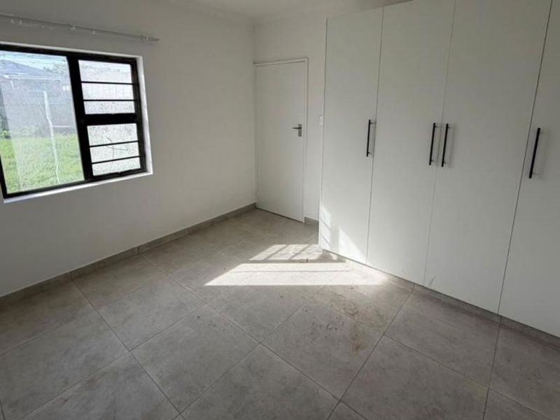 A bright, empty bedroom featuring neutral tiled flooring and extensive built-in cupboard storage with modern handles.