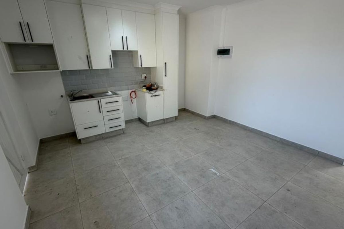 An open-plan kitchen area featuring white cabinetry, subway tile backsplash, and neutral floor tiles. The space is vacant and ready for customization.
