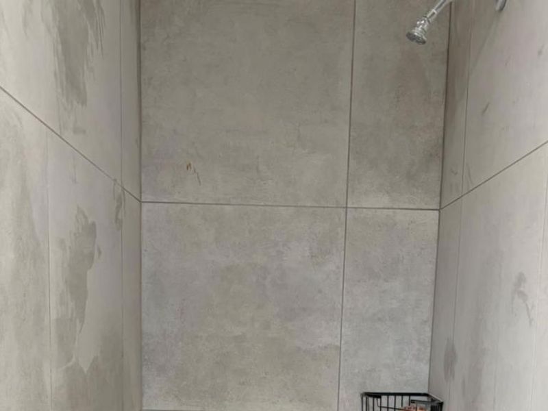 A minimalist shower enclosure featuring large format light grey wall tiles and a fixed shower head.