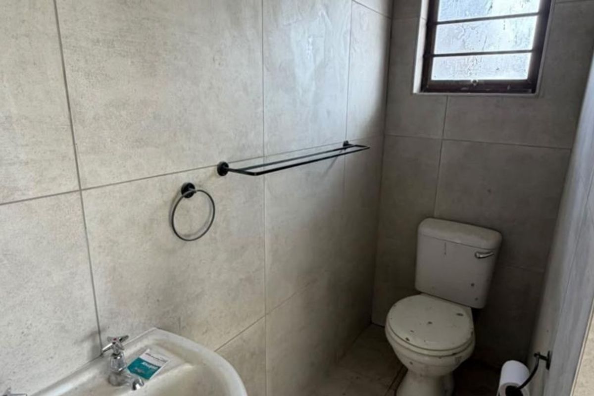 A compact bathroom featuring neutral wall tiles, a standard toilet, and a basin with modern black hardware accessories.