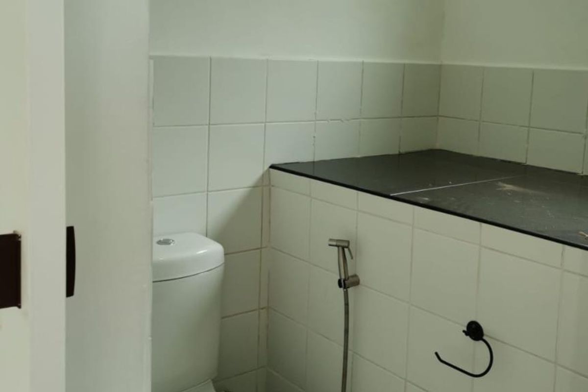 A small bathroom featuring tiled walls, a toilet, and a stone countertop, currently requiring completion of plumbing fixtures.