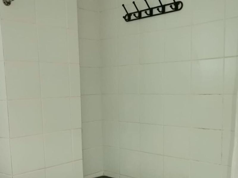 A basic bathroom area featuring white wall tiles and wall-mounted hooks, currently in need of cosmetic updates and maintenance.