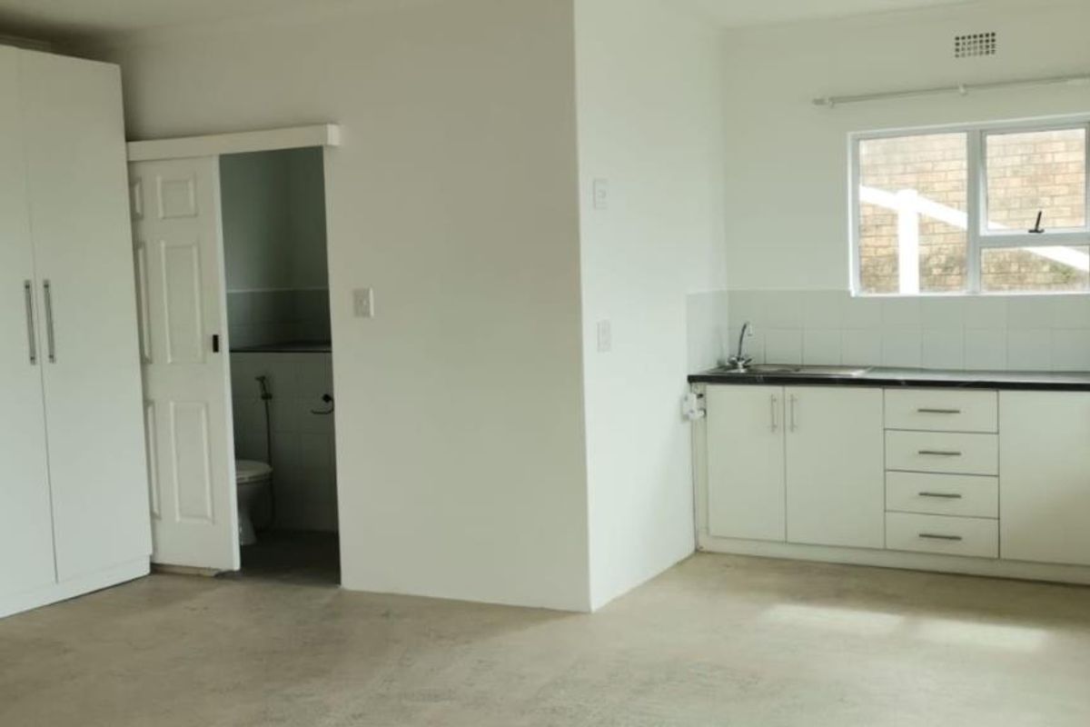 A functional kitchen area featuring white cabinetry, dark countertops, and a built-in wardrobe, with an adjacent doorway leading to a bathroom.