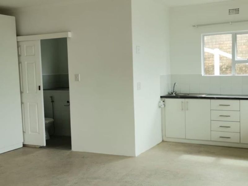 A functional kitchen area featuring white cabinetry, dark countertops, and a built-in wardrobe, with an adjacent doorway leading to a bathroom.