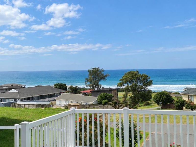 A scenic elevated view overlooking the coastline and ocean, featuring a white vinyl balcony railing and partial view of the building's brick exterior.