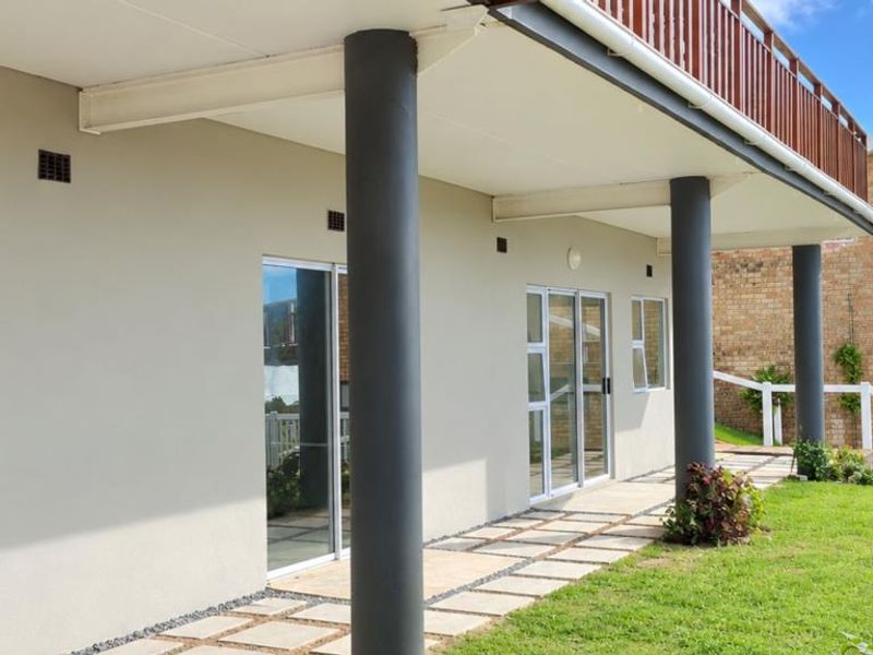 A covered patio area featuring structural columns, sliding glass doors, and a paved walkway leading to the garden.
