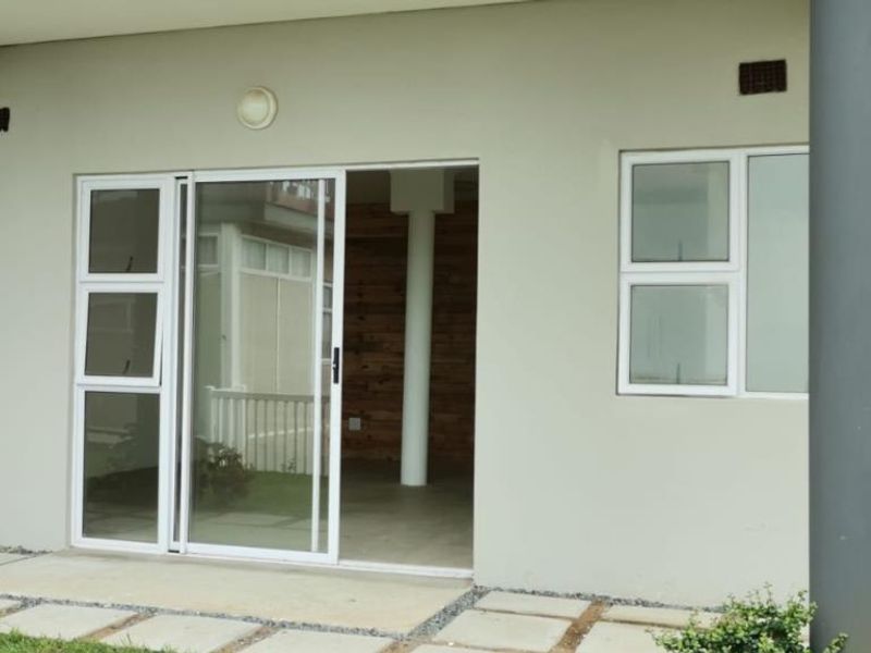 A clean exterior patio area featuring modern sliding glass doors, aluminium window frames, and concrete paving, providing seamless access to the interior living space.