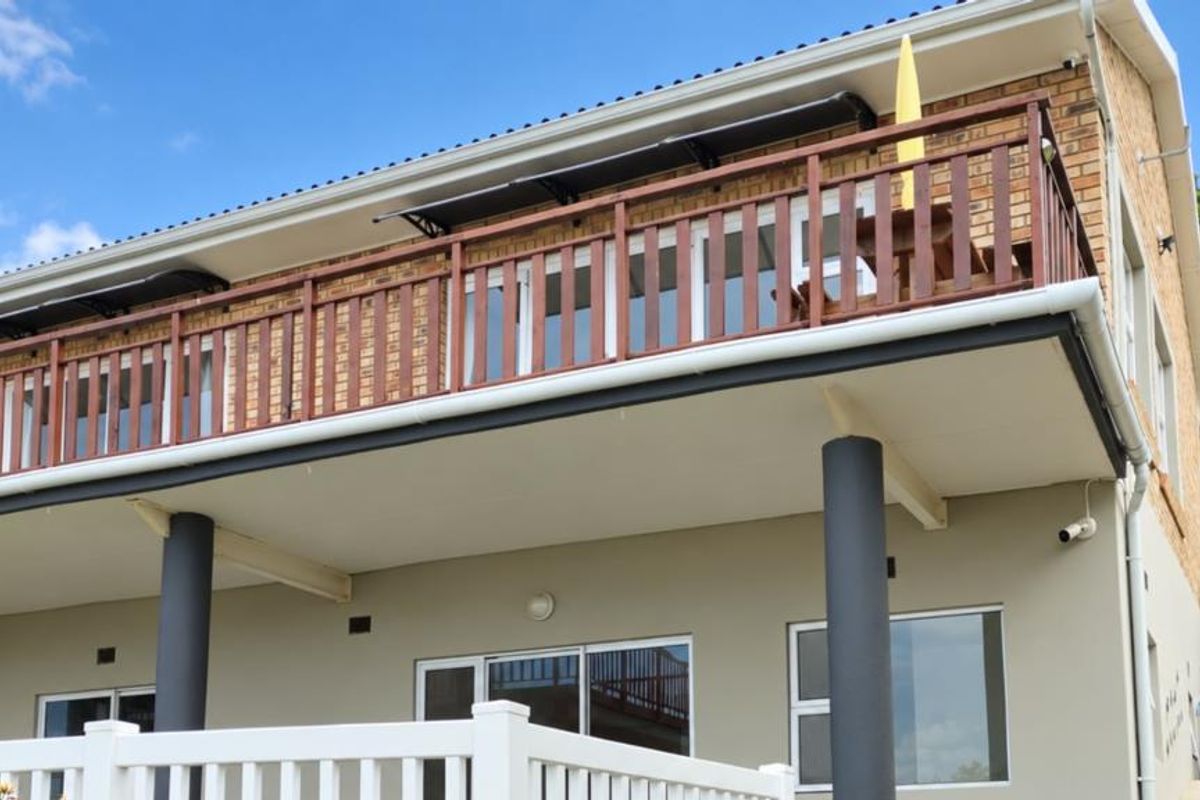 Rear view of the apartment building featuring a spacious balcony with wooden balustrades, sliding glass doors, and structural support columns.
