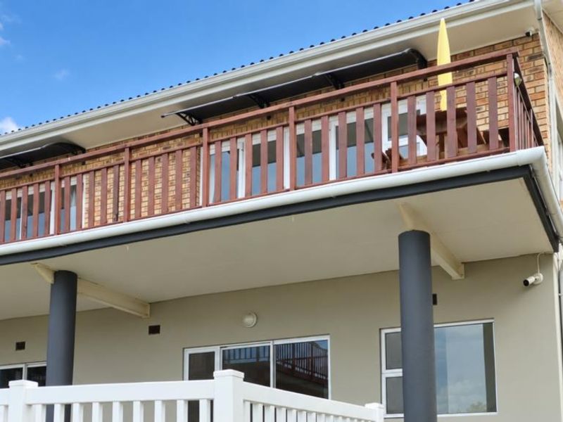 Rear view of the apartment building featuring a spacious balcony with wooden balustrades, sliding glass doors, and structural support columns.