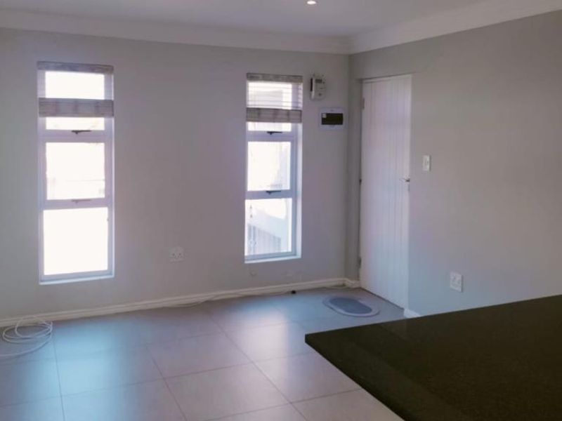 An open-plan living area featuring neutral tiled flooring, recessed downlights, and a dark granite countertop, offering a clean and versatile space.