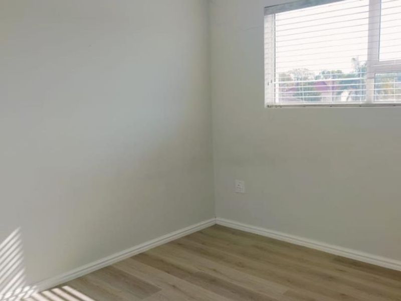 An empty bedroom featuring light-toned laminate flooring, neutral walls, and a window fitted with venetian blinds.